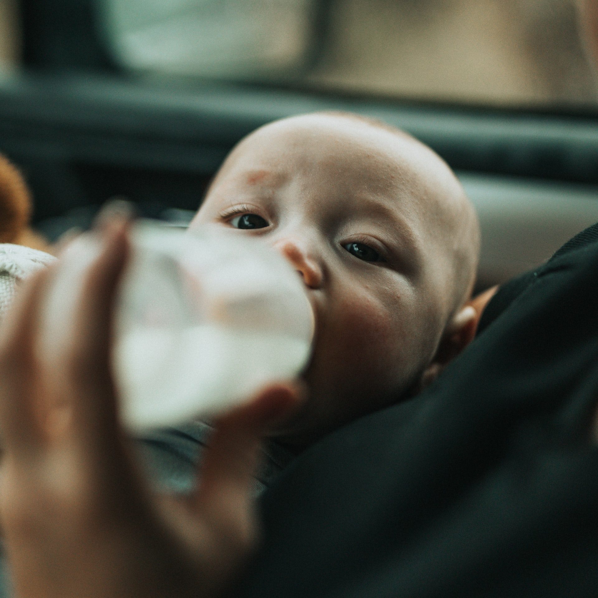 baby in blue shirt drinking milk from feeding bottle
